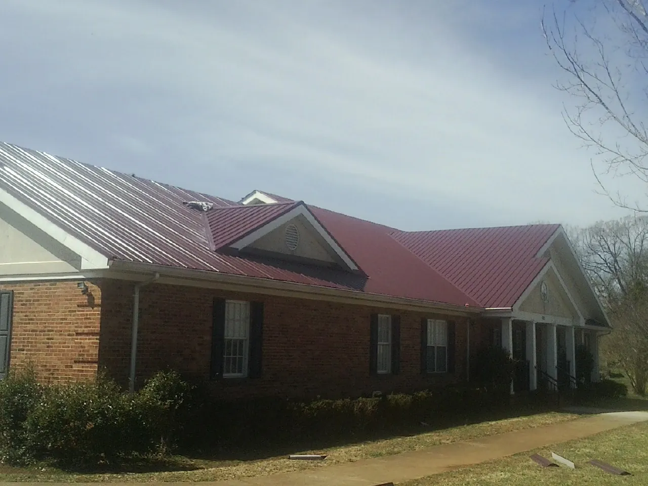 Red metal roof with gabled entries on a long brick building, from a Hail Damage Roof Repair job in West Liberty
