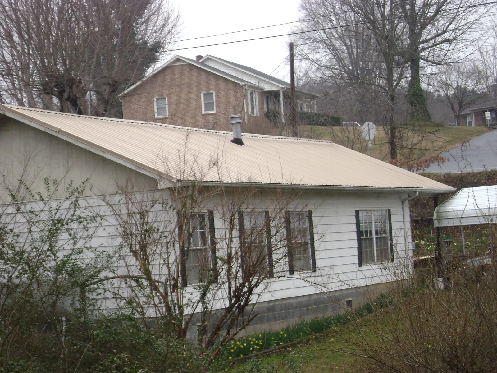 Tan metal roof on a white sided house set into a hillside — Commercial Roofing by Roofing Brothers in West Liberty